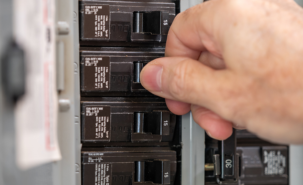 A person flipping the ON/OFF switch of a circuit breaker in an electrical panel.