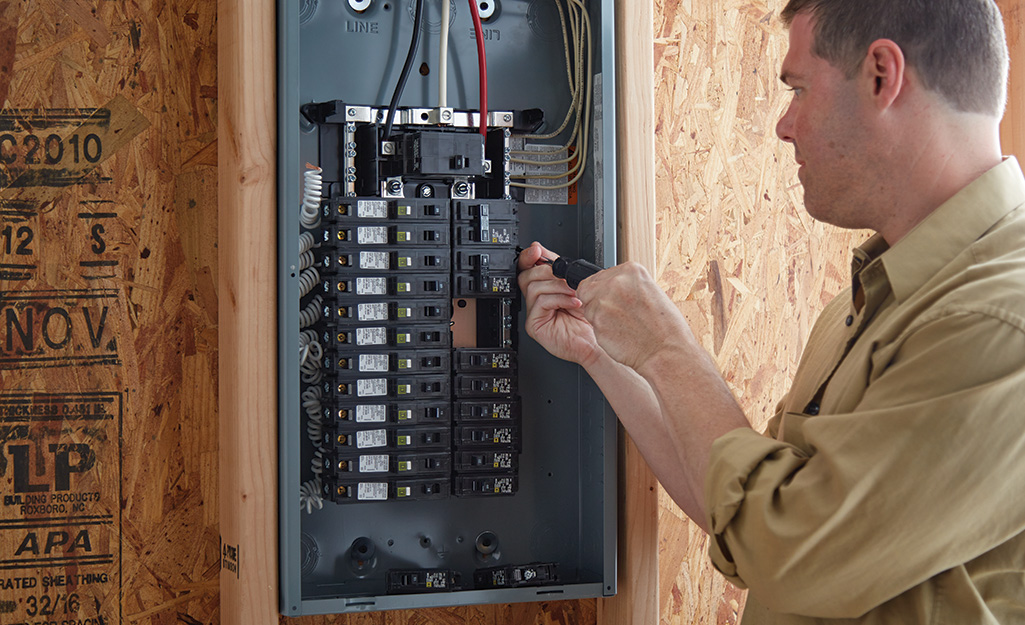 A man installing a circuit breaker in an electrical panel.