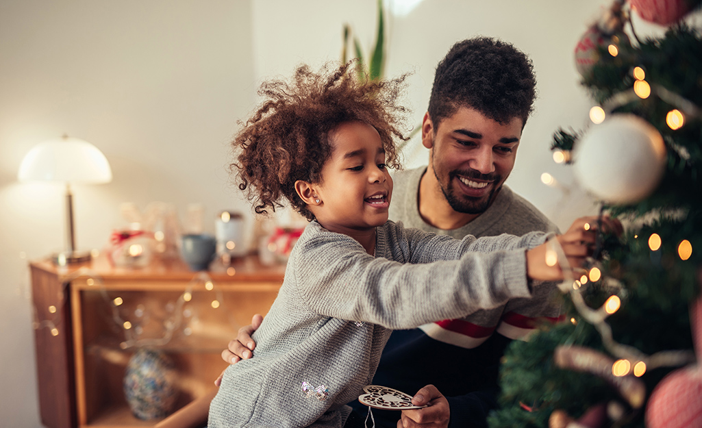 Child and dad are trimming the tree.