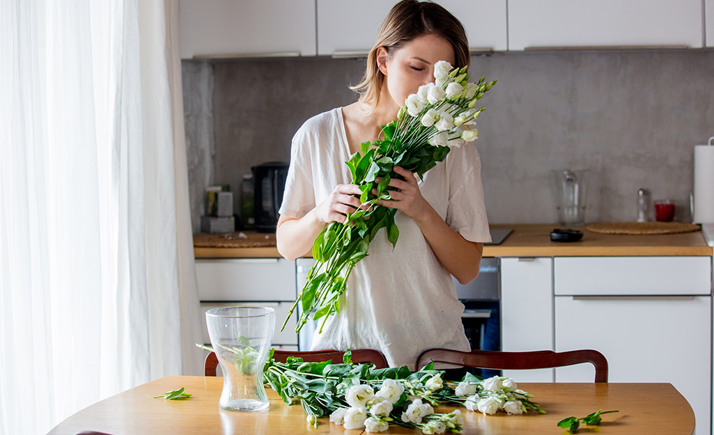 A woman holds a bunch of white roses up to her nose as she gets ready to put them in a vase.