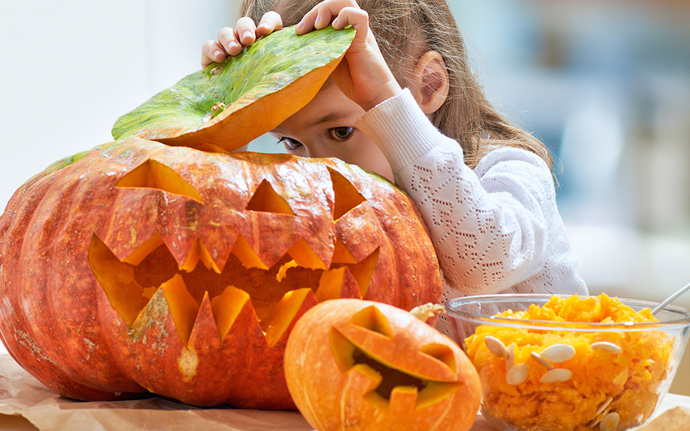 A man wearing rubber gloves carves into a pumpkin on a back porch.