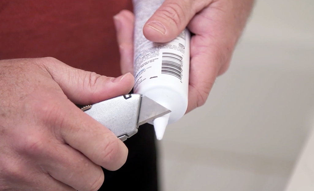 A person uses a utility knife to cut the nozzle of a caulk tube.