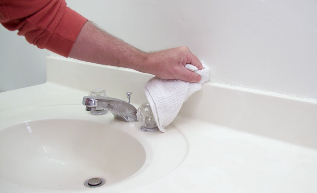 A person wipes away excess caulk on a bathroom vanity.