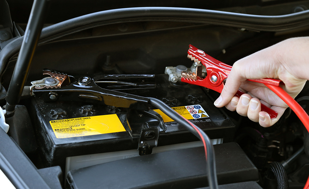 A person applies jumper cables to a car battery.