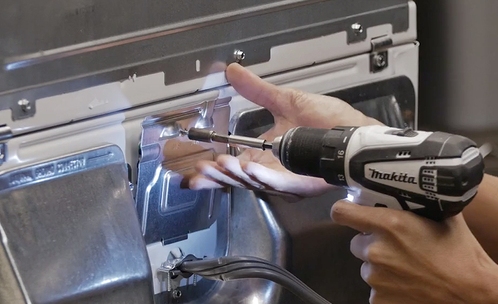 A person using a power drill to open the access panel on the back of a dryer.