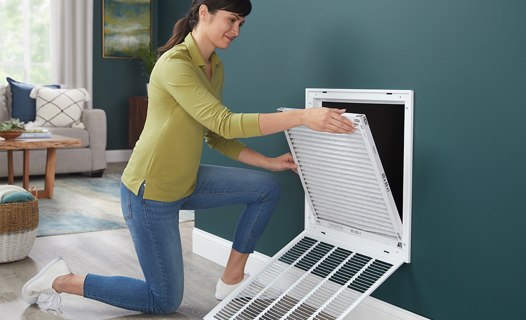 A person removing an air filter from a wall vent.