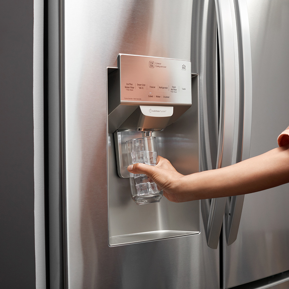 A person gets water from a dispenser in a refrigerator door.