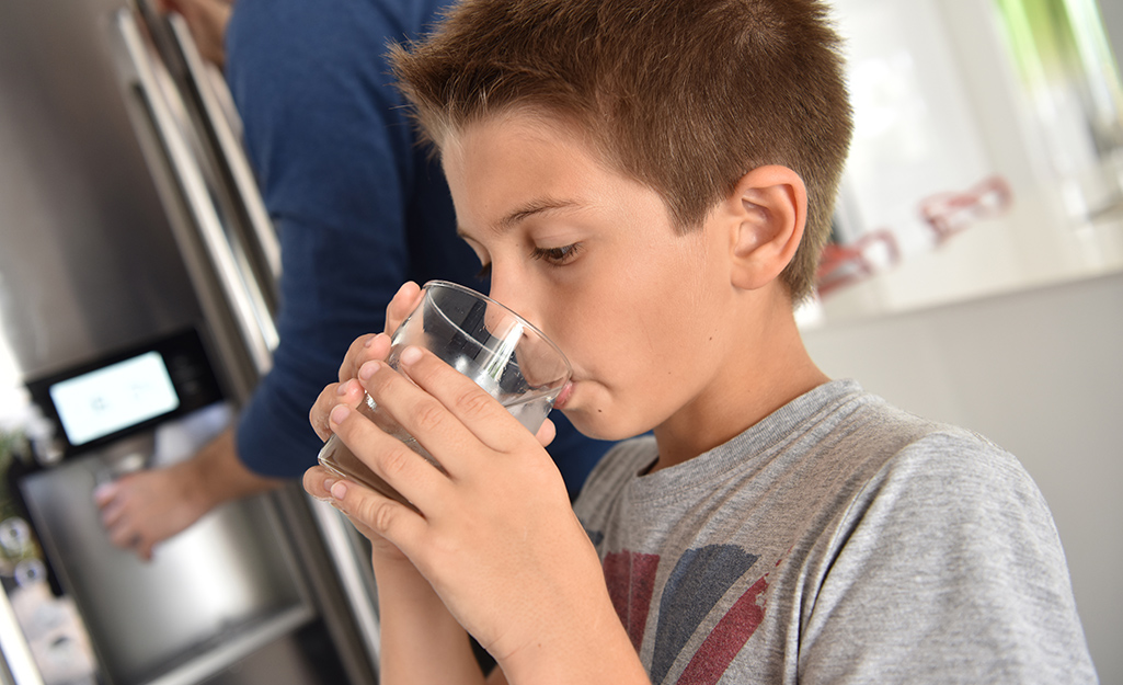 A kid drinking a glass of water from the fridge.
