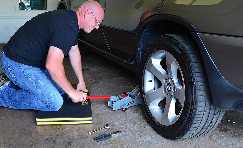 A person uses a jack to raise a car tire. 