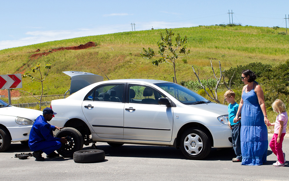 A family waits while a service person performs roadside assistance. A family waits while a service person performs roadside assistance.