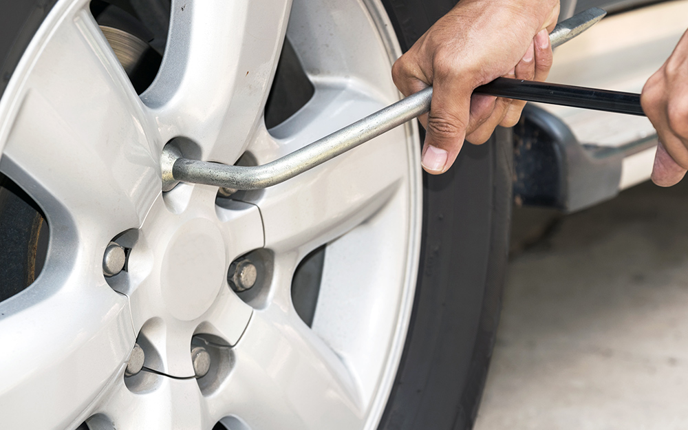 A person uses a tire iron to remove lug nuts from a wheel.