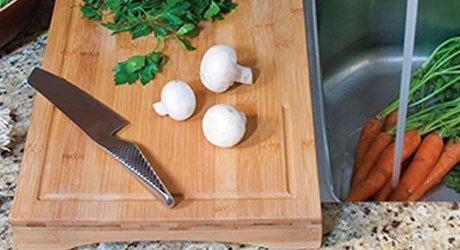 A bamboo cutting board with a knife and vegetables.