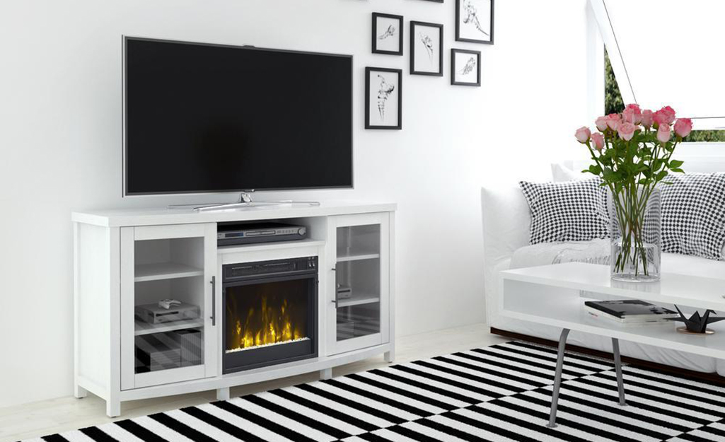 A white fireplace TV stand sits at the edge of a black and white striped rug in a living room.