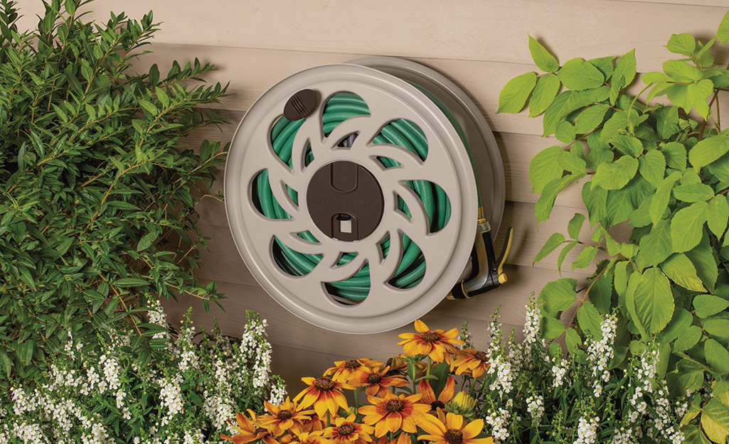 A garden hose is wound on a hose reel that's mounted on house siding.