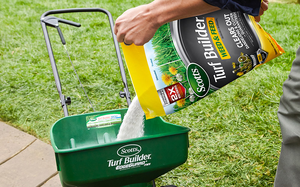 Person putting weed-and-feed fertilizer into a spreader.