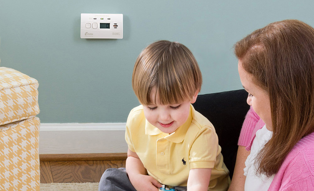 An adult playing with a child near a carbon monoxide alarm installed nearby.