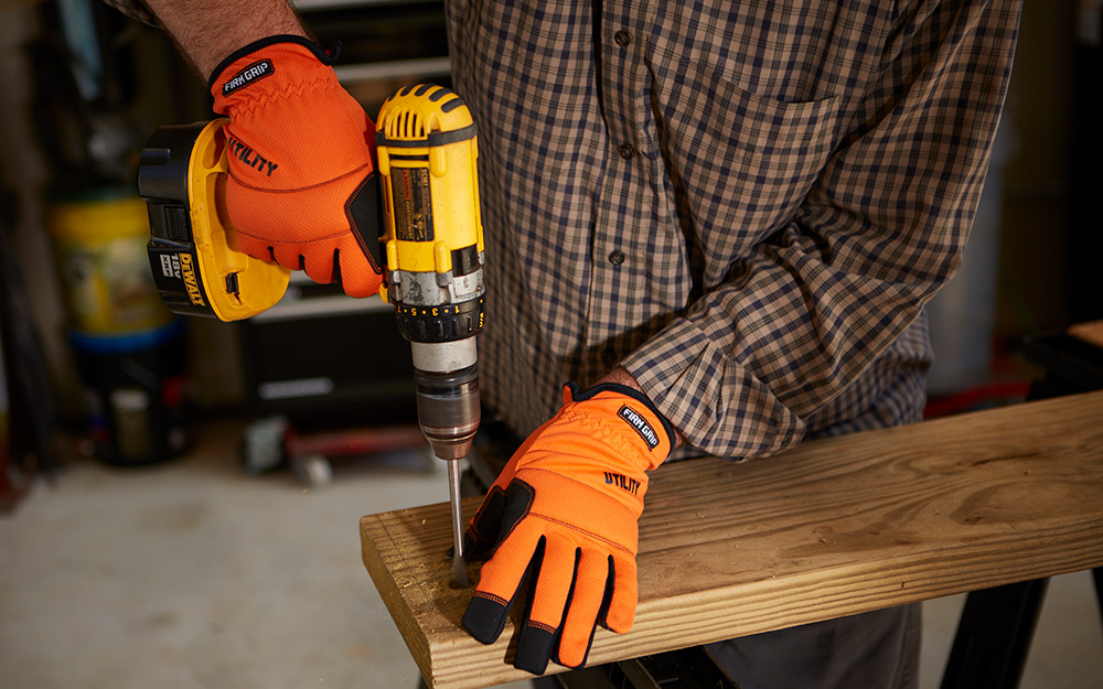 A person wearing gloves while using a drill