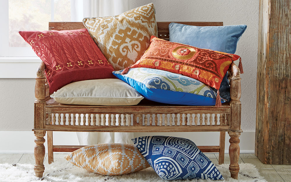 A hand-carved wood settee stacked high with orange, blue and tan pillows.