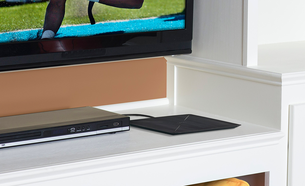 An HD antenna lays on top of shelf below a television.