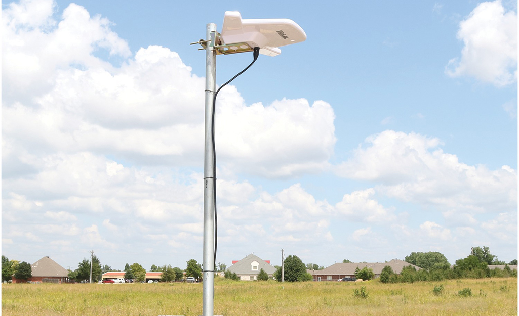 An outdoor amplified HD antenna stands in a field with houses in the background.