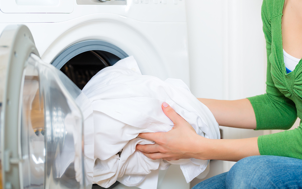 A woman loads sheets into a washing machine. 