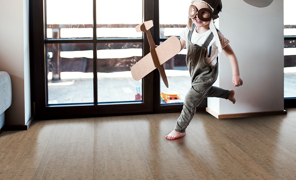 A child dressed as a pilot holds a toy plane while running over cork floors.