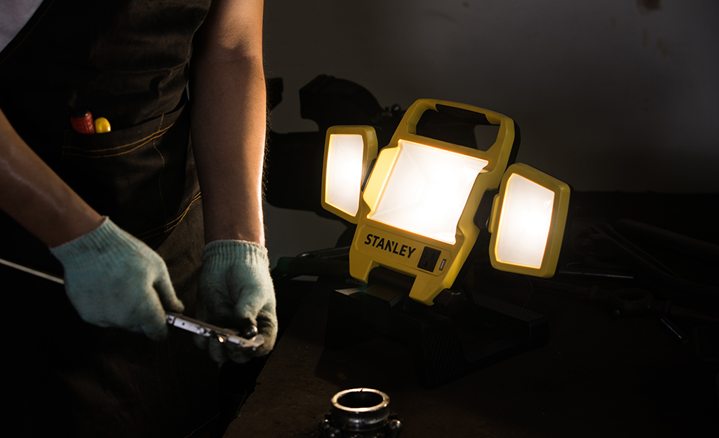 A person uses a portable garage light to do work.