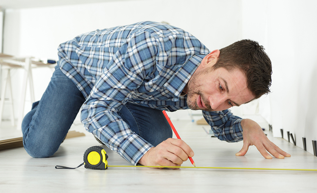 A person measures the size of a room with a tape measure.