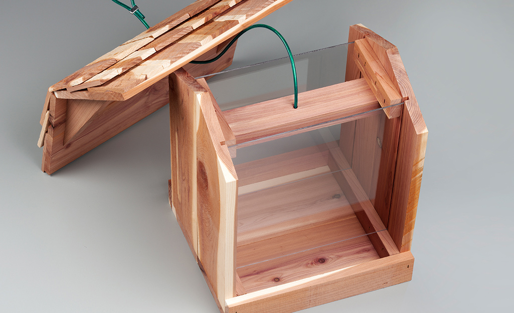 The roof of a wooden bird feeder leans against the main part of the feeder.