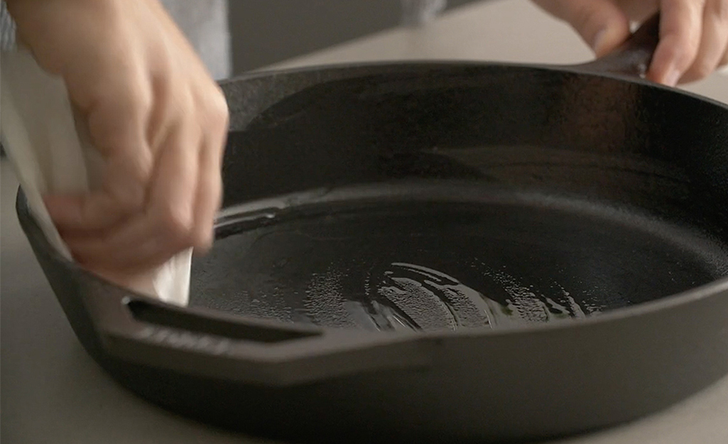 A person applies oil to a cast iron skillet.