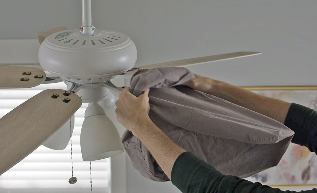 A person inserts a ceiling fan blade into a pillowcase.