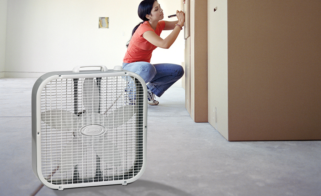 A person working in a room with a box fan.
