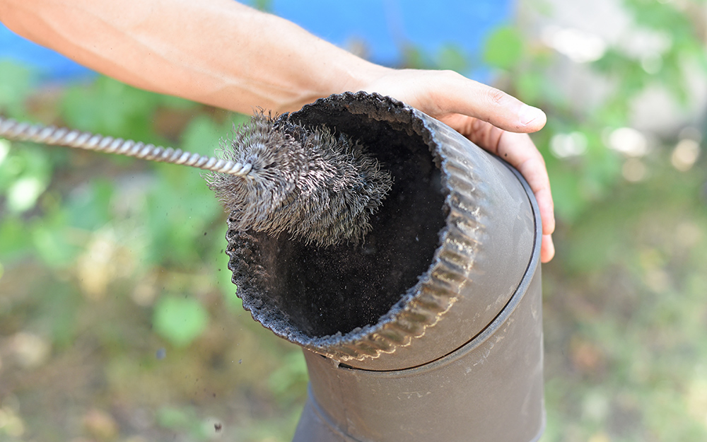 A person cleans the inner top of a chimney with a brush.