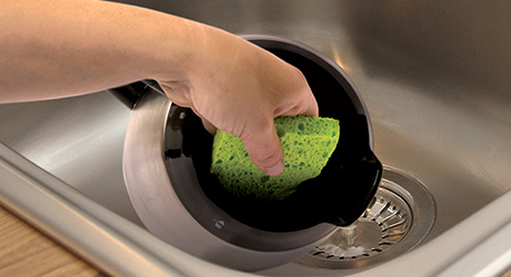 A person uses a sponge to clean the inside of a coffee pot.
