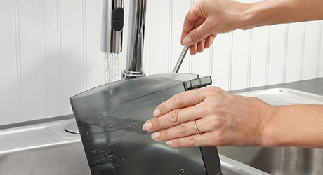 A person runs water from a faucet to clean the water tank of a coffee maker.