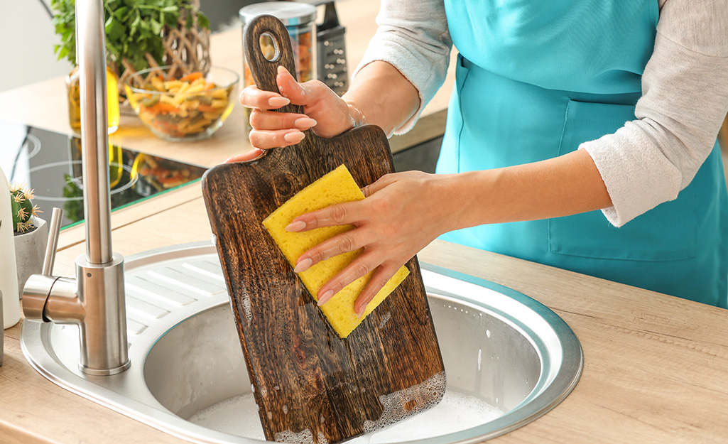 A woman washes a wooden cutting board with soapy water in a sink.