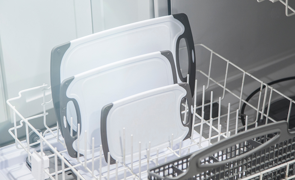 Three white plastic cutting boards stand in the rack of a dishwasher.