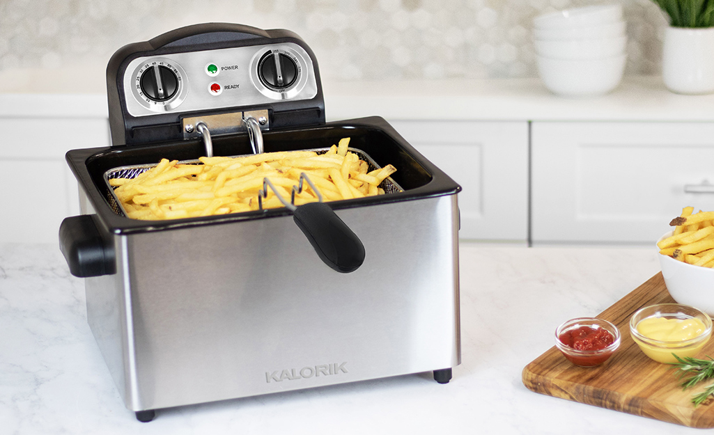 French fries fill the basket of a deep fryer on a countertop.