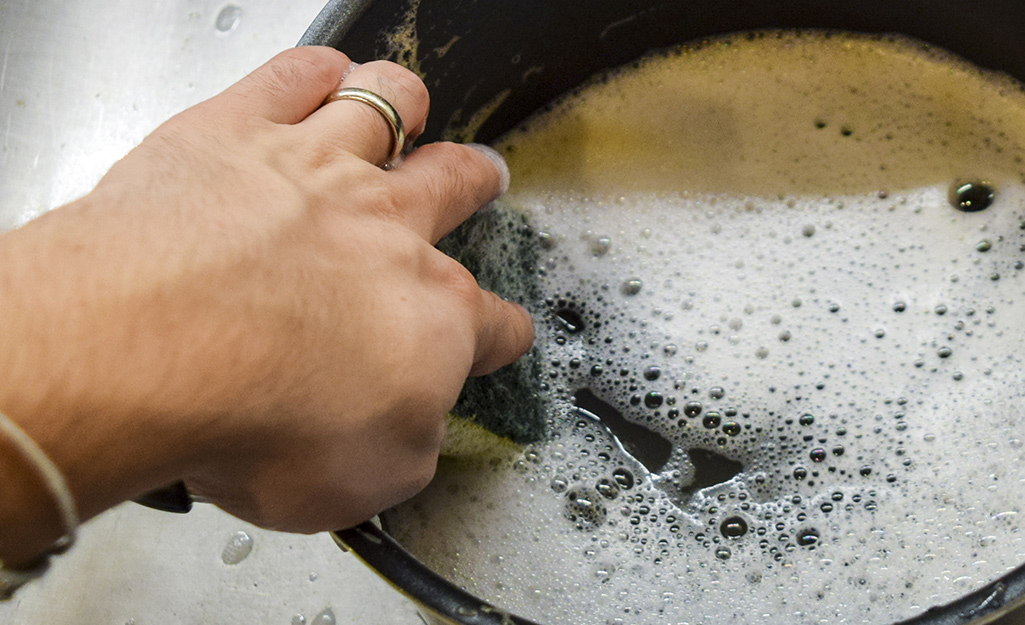 A person wipes the inside of a deep fryer filled with soapy water.