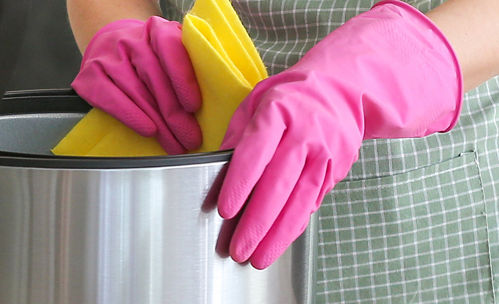 A person wearing gloves wipes down the inside of a deep fryer.