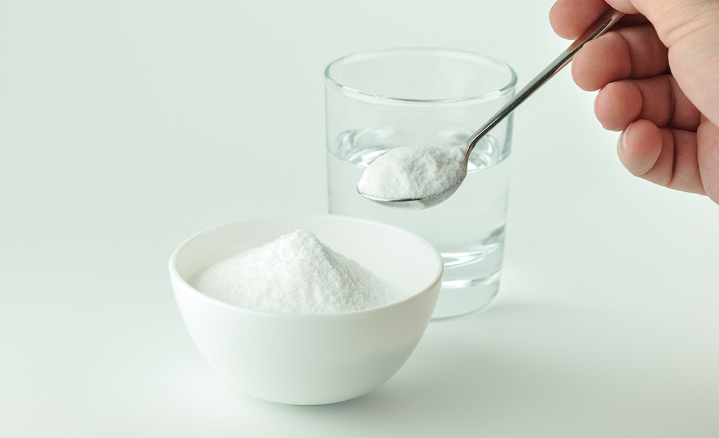 A person holds a spoonful of baking soda next to a glass of water.