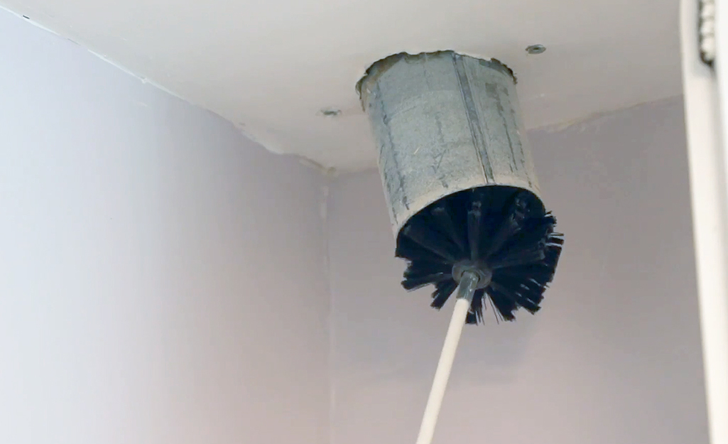 A person uses a flexible brush to clean the inside of a clothes dryer vent.