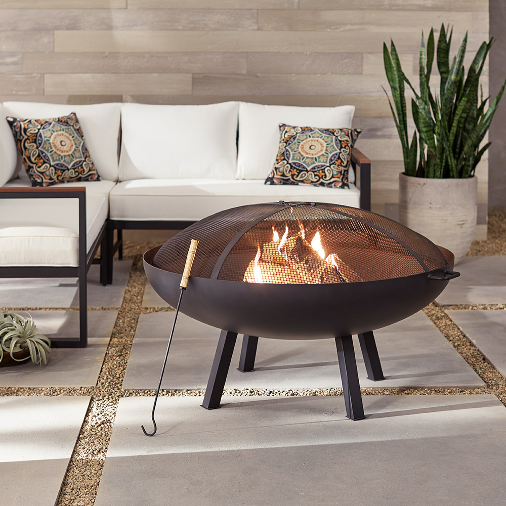A fire pit stands on a patio in front of an outdoor seating area.
