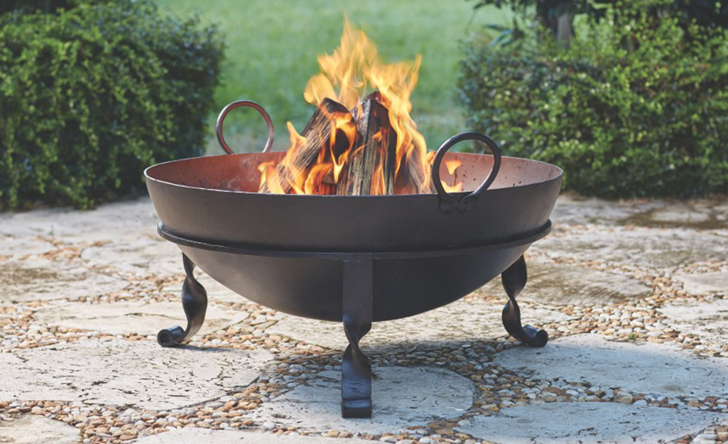 A fire burns inside of a cast iron fire pit on a patio.