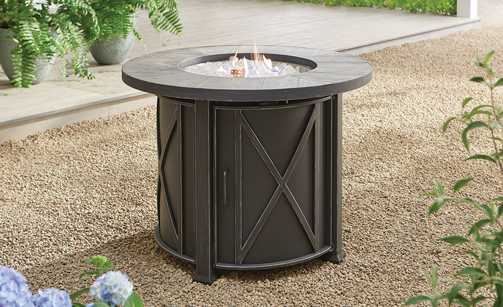 A gas fire pit stands on top of crushed stone.
