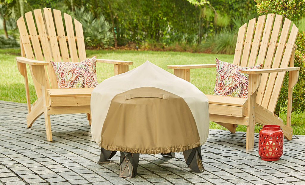 A covered fire pit stands in front of two chairs on a patio.
