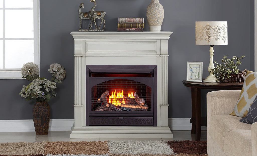 A fire burns in a gas fireplace with a white mantle against a gray wall.
