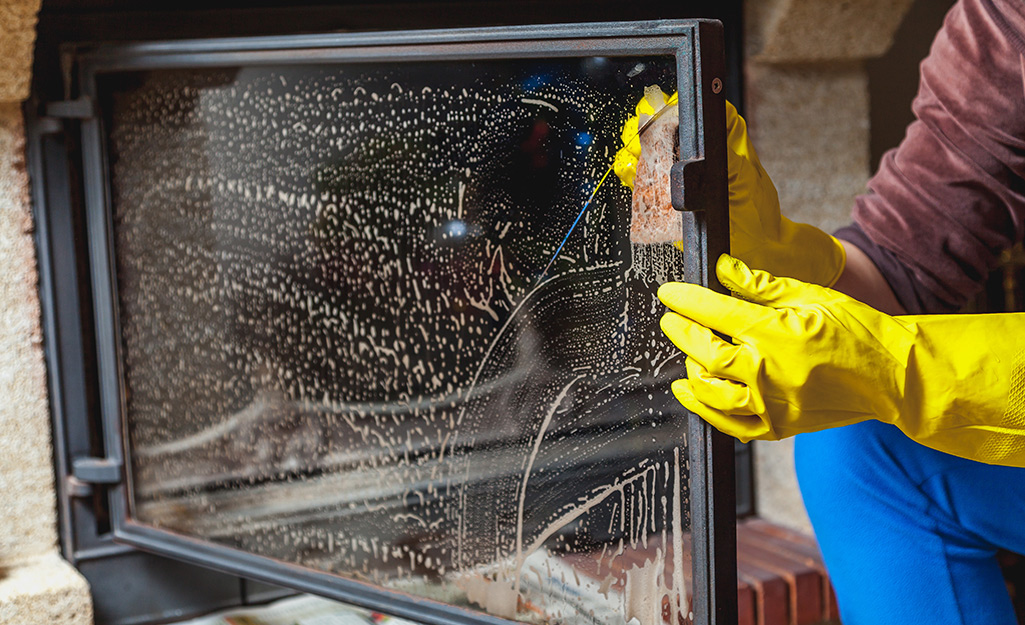 A person cleans the inside of a glass fireplace screen.