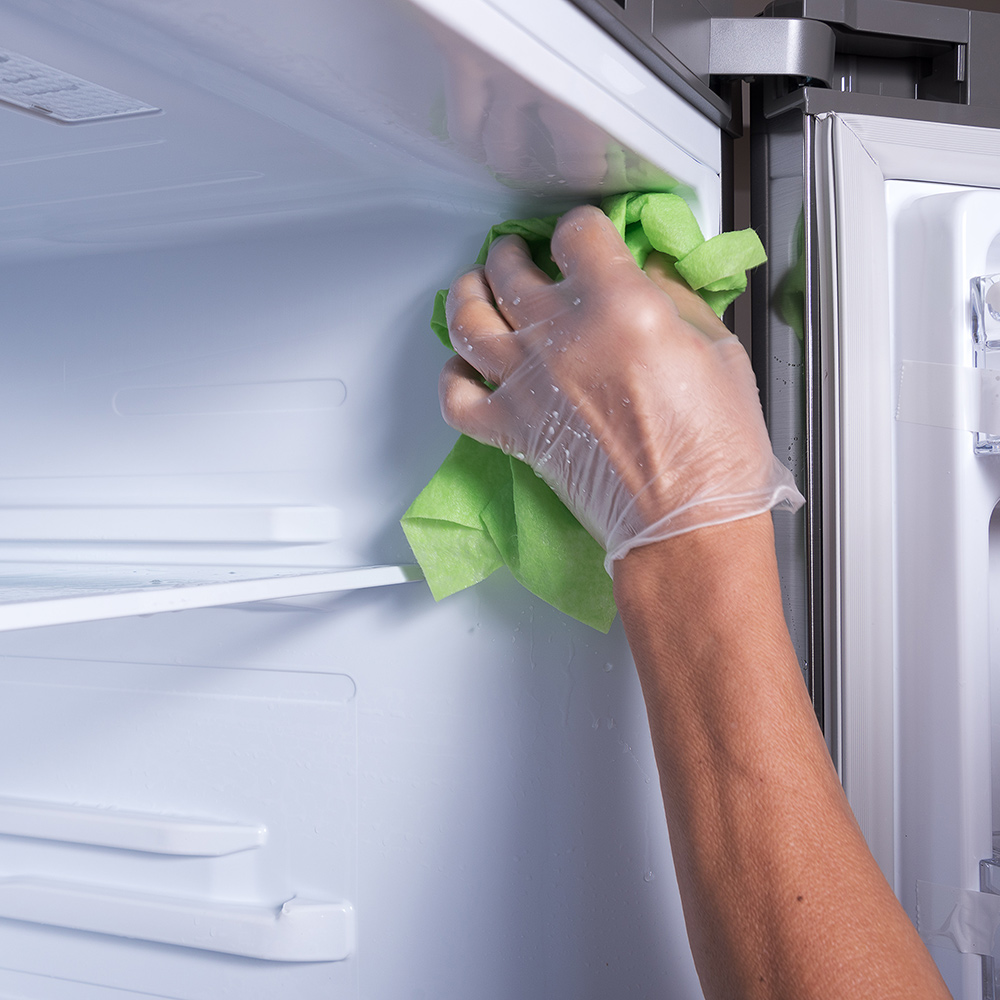 A person wears a glove to clean a freezer with a cloth.