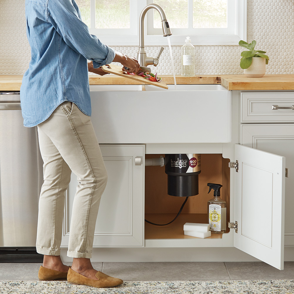 A person at a kitchen sink preparing to use a garbage disposal